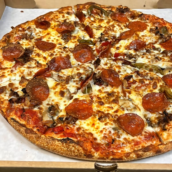 A close-up of a South St Pizzeria pizza, topped with pepperoni, sausage, peppers, and melted cheese.