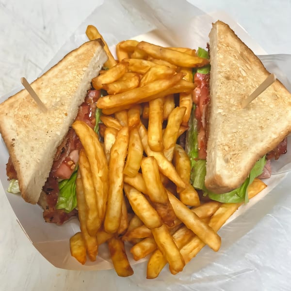A club sandwich with bacon, lettuce, and tomato, served with a side of golden french fries.