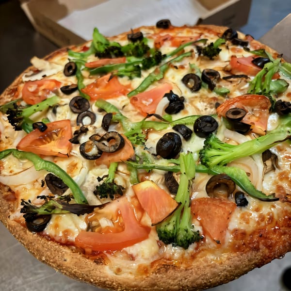 A South St Pizzeria pizza with tomatoes, black olives, broccoli, onions, and green peppers.