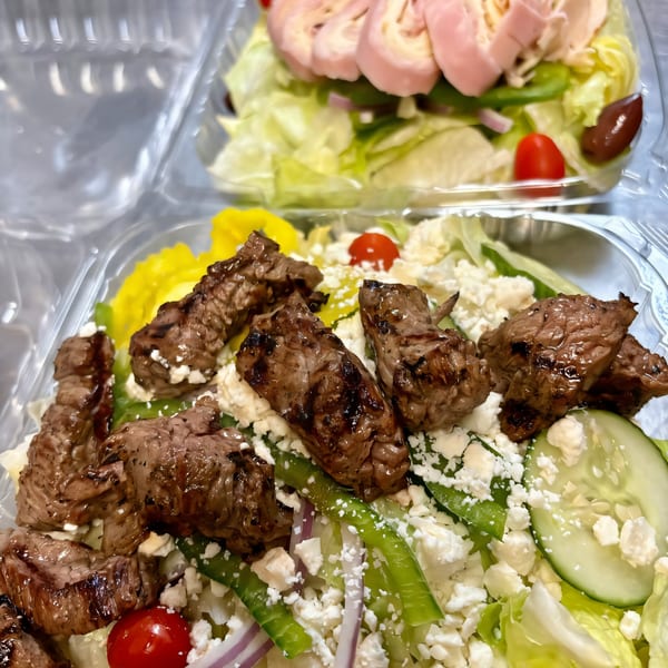 Two plastic containers of salads, one with steak and feta, the other with rolled ham and olives.