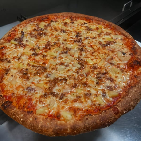 A freshly baked South St Pizzeria pizza, topped with melted cheese, pineapple, and ground meat.