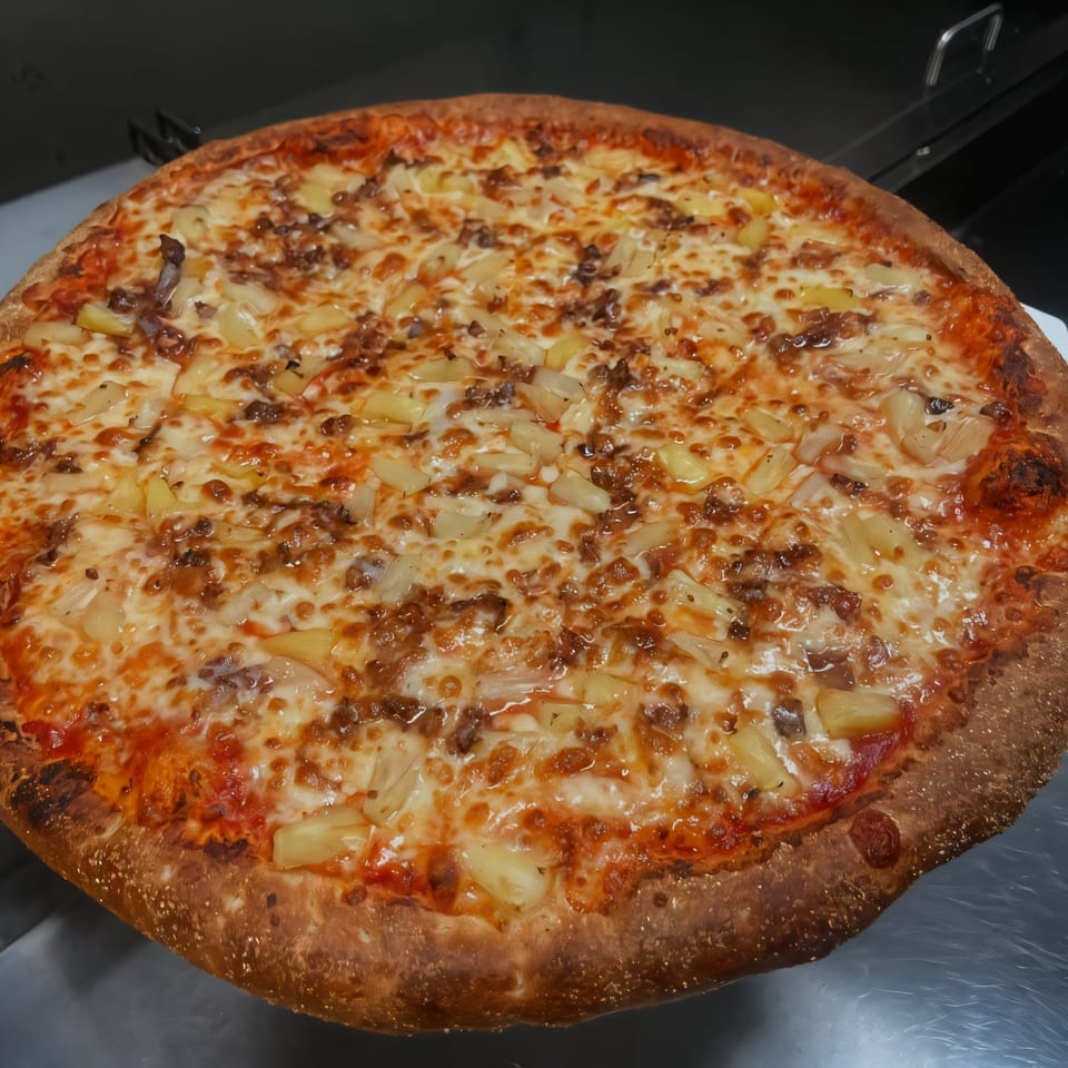 A freshly baked South St Pizzeria pizza, topped with melted cheese, pineapple, and ground meat.