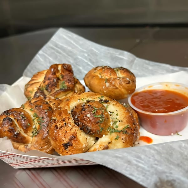 Garlic knots with herbs and salt, served with a side of marinara sauce in a paper tray.
