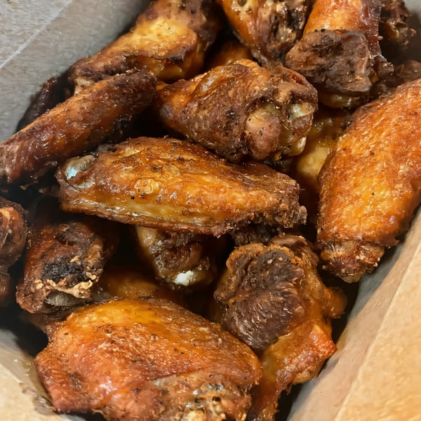Close-up of South St Pizzeria's crispy, golden-brown chicken wings, glistening with sauce in a cardboard box.